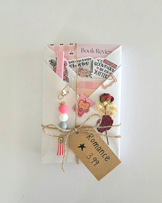 A book wrapped in white kraft paper with twine, decorated with pink elements, a small dried rose wax sealed to the wrapping, and a brown paper tag that reads 'Romance 3.99 stars.'