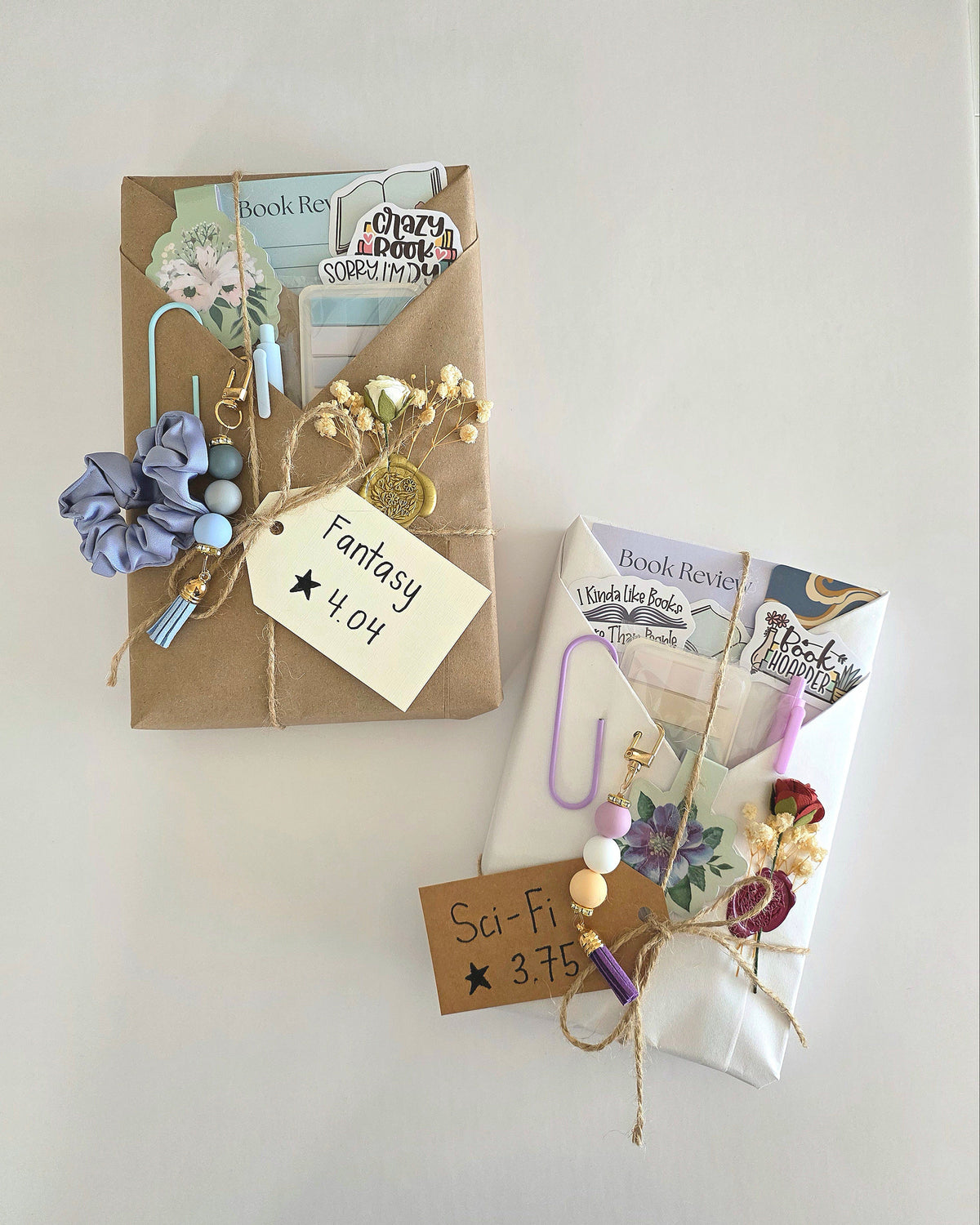 Two wrapped books decorated with handmade paper tags, ribbons, keychains, stickers, flower embellishments, and wax seals arranged on a plain light background.